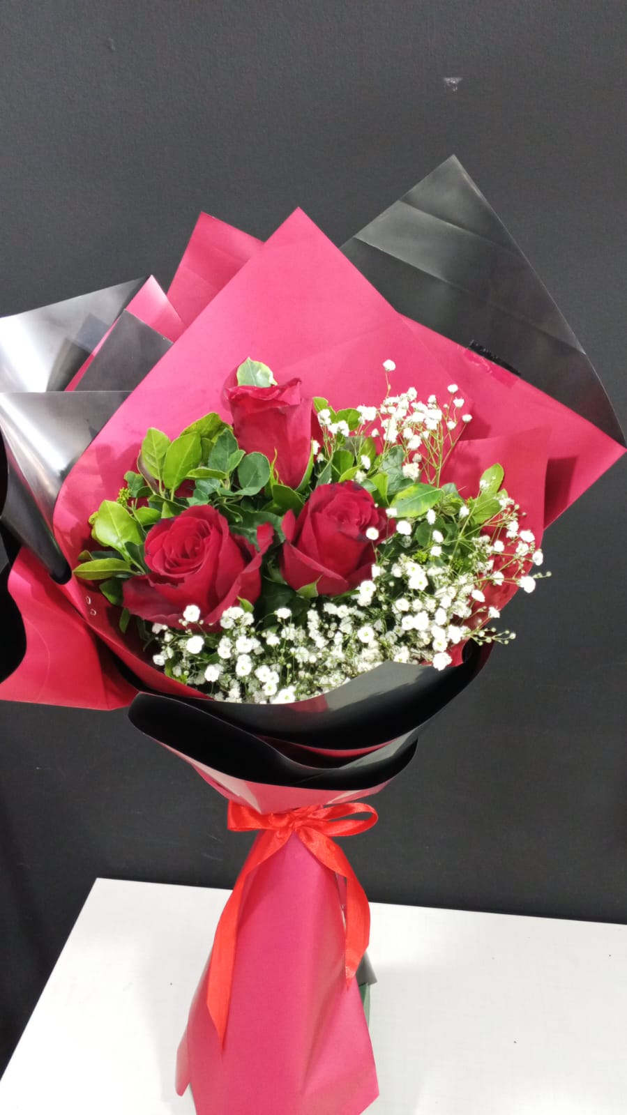 Three red roses with baby's breath in pink and black wrapper